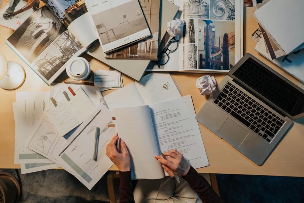 Overhead view of a work desk with documents, laptop, and creative materials.